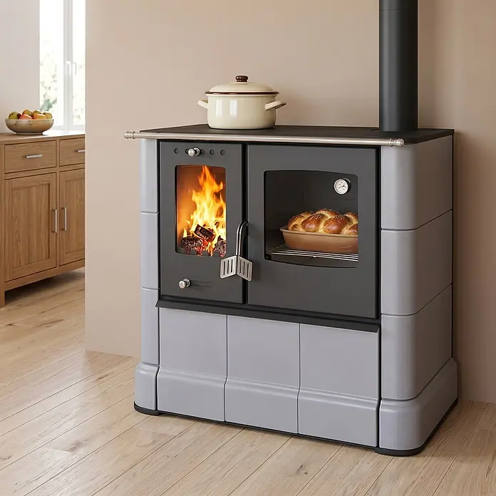 Domofire Kaminofen Sparherd Steyr M - 7,5 kW, Raumheizvermögen: 150 m³, Material Verkleidung: Keramik, Schwarz - Hellgrauer und schwarzer Holzofen mit brennendem Feuer und backendem Brot im Ofen, ein Topf obenauf, in einer Küchenumgebung.