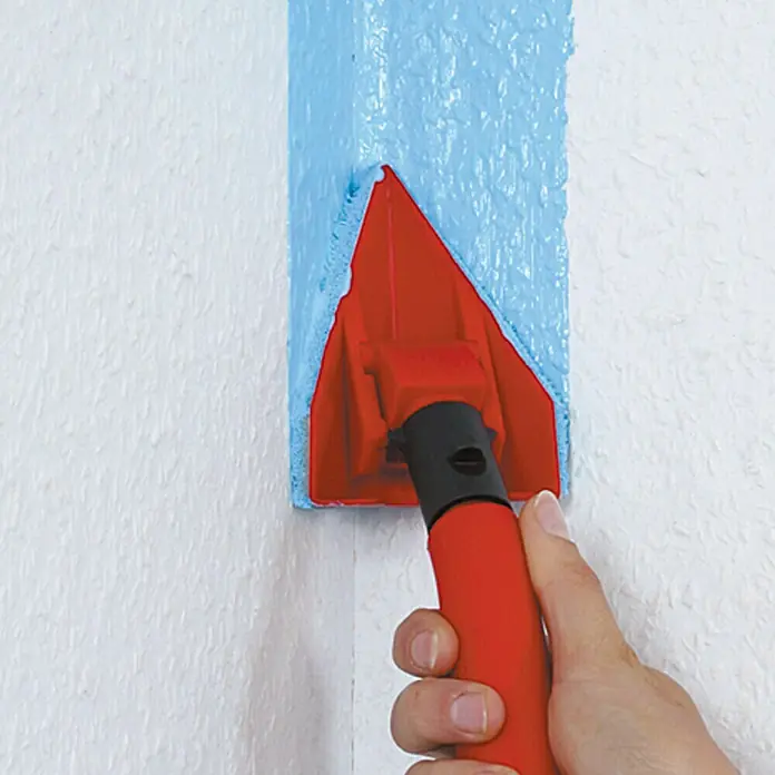 Lehnartz Isi-Line Eckenstreicher - Maße Kissen: 100 x 85 mm, Schwenkbarer Streichkopf - Nahaufnahme eines roten Eckrollers beim Auftragen von blauer Farbe auf eine weiße Wand.