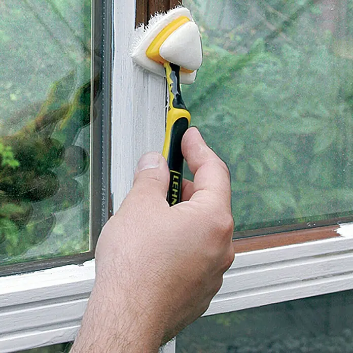 Lehnartz Isi-Line Streicher-Set Premium Delta 3-in-1 - 5 -tlg. - Detailaufnahme eines Fensterreinigers in Aktion, der Fensterrahmen säubert. Das Werkzeug hat einen gelb-schwarzen Griff.