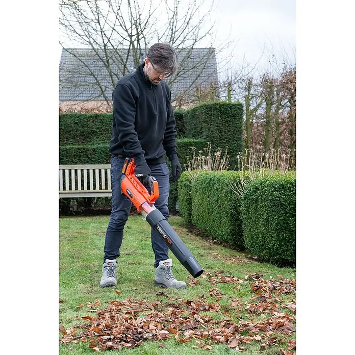 PowerPlus Soplador de batería POWDPGLBS1 - 20 V, 1 batería, 2 Ah, Velocidad de soplado: 145 km/h - Hombre en un jardín usando un soplador de hojas naranja y negro para limpiar hojas caídas.