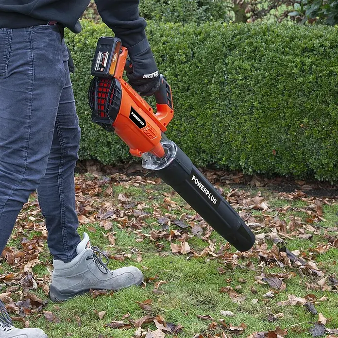 PowerPlus Soplador de batería POWDPGLBS1 - 20 V, 1 batería, 2 Ah, Velocidad de soplado: 145 km/h - Soplador de hojas inalámbrico naranja y negro en uso, operado por una persona en un césped con hojas.