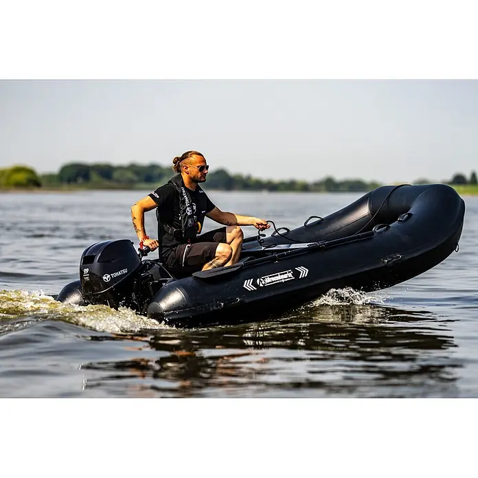 Tohatsu Schlauchboot-Set MFS 5 DDS Motor & Allroundmarin T320 Schlauchboot - Motorleistung: 3,7 kW - Mann steuert ein schwarzes Schlauchboot mit Tohatsu Außenborder auf dem Wasser.