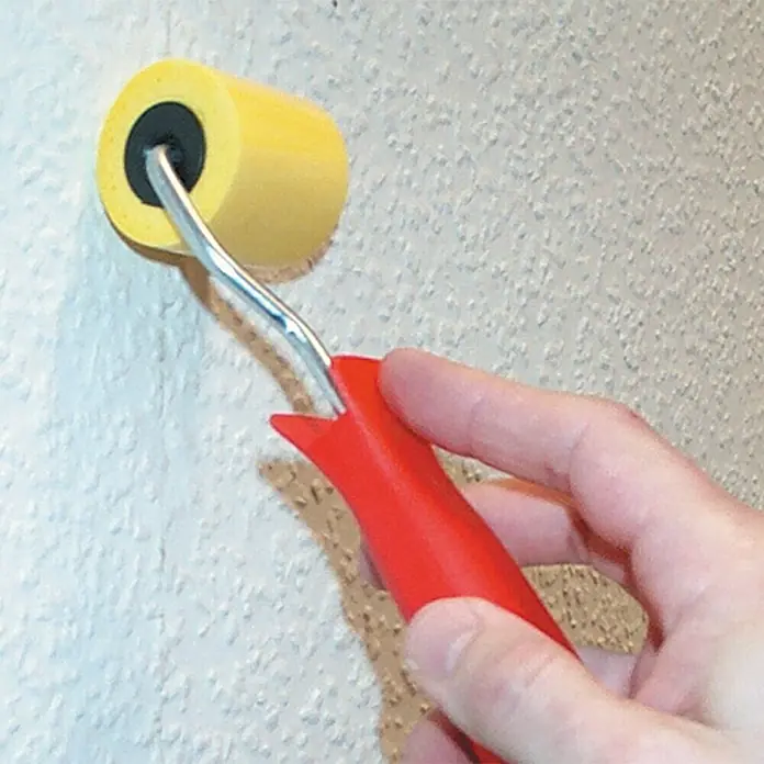 Lehnartz Tapezier-Set - 6 -tlg. - Nahaufnahme einer Hand, die eine gelbe Farbwalze mit rotem Griff zum Auftragen von Farbe auf eine strukturierte Wand hält.