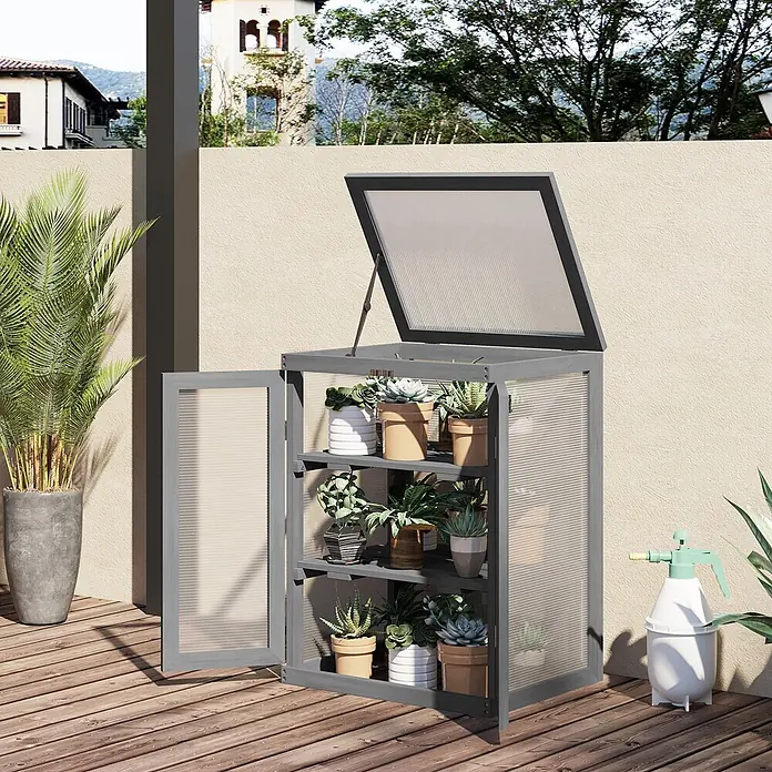 SONNENH Gewächshaus - 58 x 44 cm, Material Seitenwand: Kunststoff, Grau - Grauer Holz-Pflanzenschrank mit durchsichtigen Paneelen und Topfpflanzen, auf Holzterrasse mit geöffnetem Deckel und Tür.