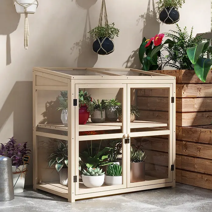 SONNENH Gewächshaus - 103 x 61 cm, Material Seitenwand: Kunststoff, Beige - Helles Holz-Minigewächshaus mit Glaspaneelen, gefüllt mit Pflanzen, auf Betonboden auf einer Terrasse.