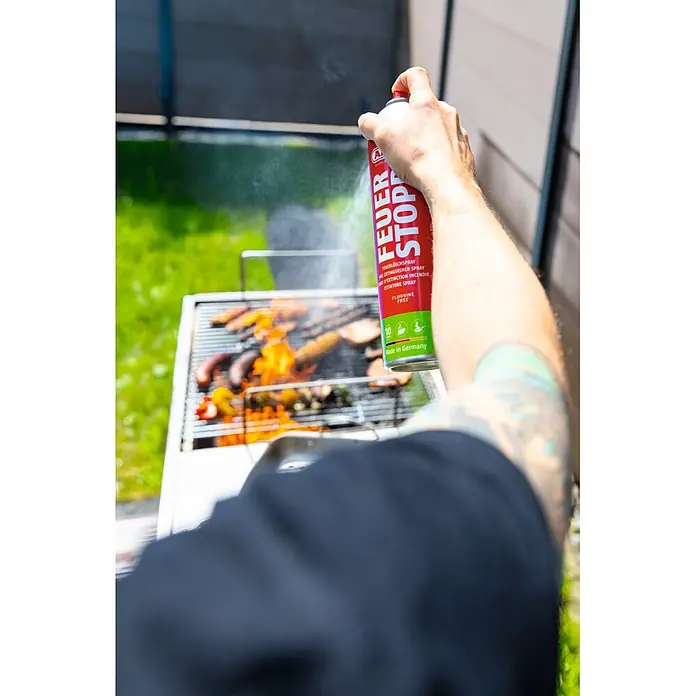 Abus Feuerlöschspray AFS625 - Geeignet für: Elektrische Anlagen bis 1.000 V (min. Abstand 1 m), 625 ml - Eine Hand hält eine rote FEUER STOP Feuerlöschspraydose und zielt auf einen brennenden Grill.