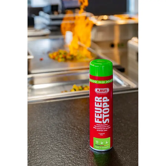 Abus Feuerlöschspray AFS625 - Geeignet für: Elektrische Anlagen bis 1.000 V (min. Abstand 1 m), 625 ml - Rote ABUS 'Feuer Stopp' Feuerlöschspraydose mit grüner Kappe, auf einer Theke vor Küchenbrand.