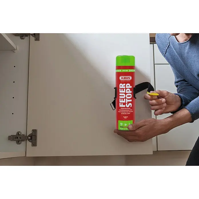Abus Feuerlöschspray AFS625 - Geeignet für: Elektrische Anlagen bis 1.000 V (min. Abstand 1 m), 625 ml - Rotes ABUS FEUER STOPP Feuerlöschspray in einer weißen Schranktür montiert, eine Hand zieht an einer gelben Lasche.