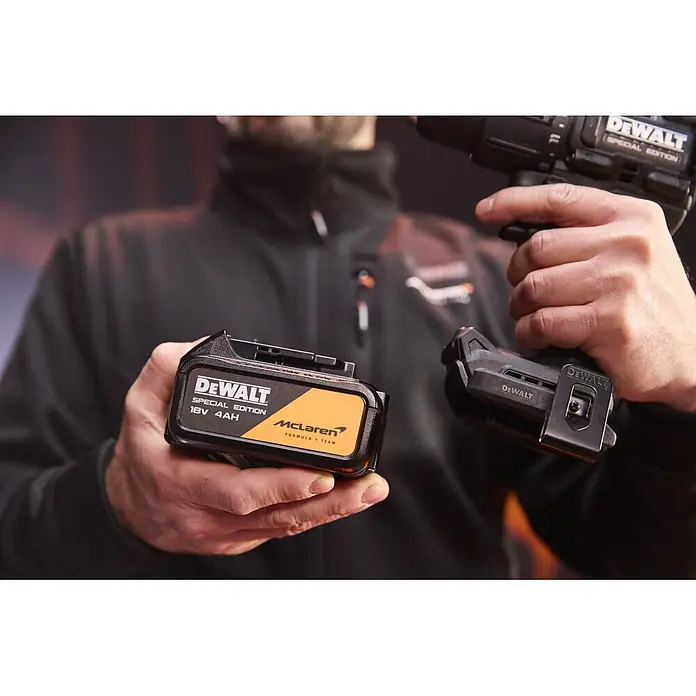 DeWalt Taladro percutor de batería McLaren DCD86MM2T - 18 V, 2 baterías, 4 Ah, 90 Nm - Batería DeWalt Special Edition McLaren (18V 4Ah, negra/naranja) y taladro a juego sostenidos por una persona.