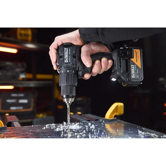 DeWalt Taladro percutor de batería McLaren DCD86MM2T - 18 V, 2 baterías, 4 Ah, 90 Nm - Una mano sostiene un taladro negro y naranja DeWalt McLaren Special Edition, perforando una superficie metálica y produciendo virutas.