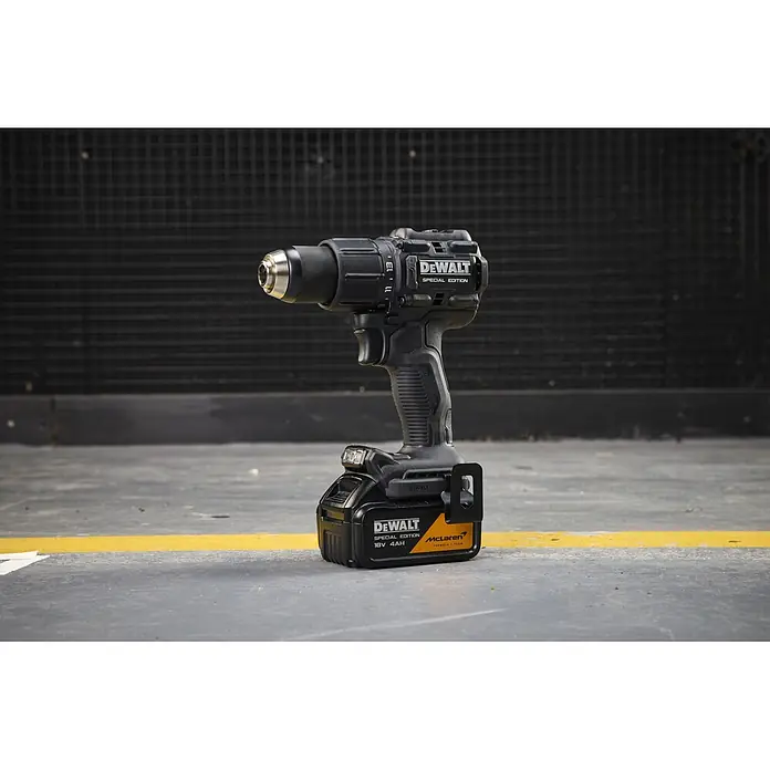 DeWalt Taladro percutor de batería McLaren DCD86MM2T - 18 V, 2 baterías, 4 Ah, 90 Nm - Un taladro inalámbrico DeWalt negro con una batería McLaren Special Edition sobre un suelo de hormigón con una línea amarilla.