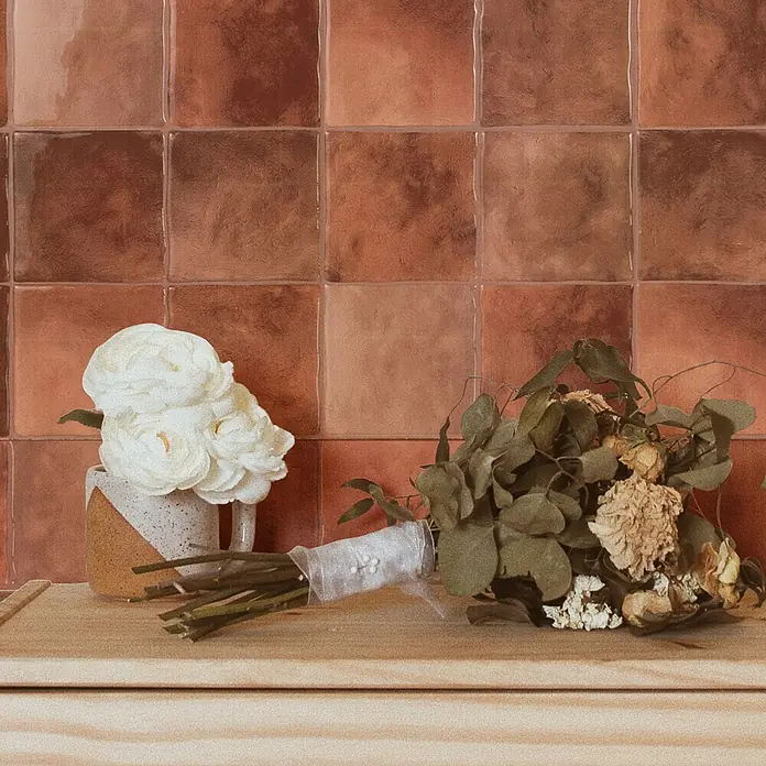 Smart Tiles Selbstklebemosaik Zellige - 22,86 x 22,86 cm, Safi, Glänzend - Ein frisches weißes Blumenarrangement in einem zweifarbigen Becher und ein getrockneter Strauß mit Spitze gebunden stehen auf einer Holzoberfläche.