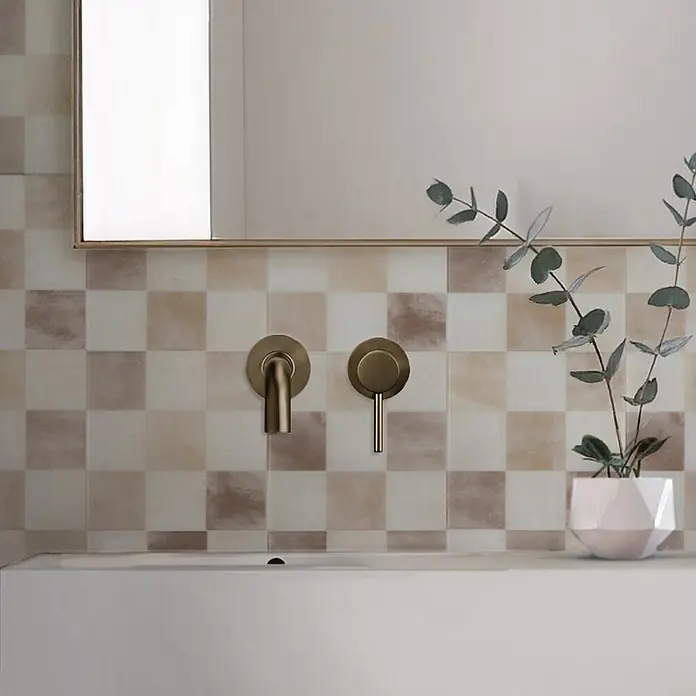 Smart Tiles Selbstklebemosaik Damier - 19,69 x 19,69 cm, Luxor, Matt - Bronzene Wandarmatur mit separatem Griff über einem Waschbecken.