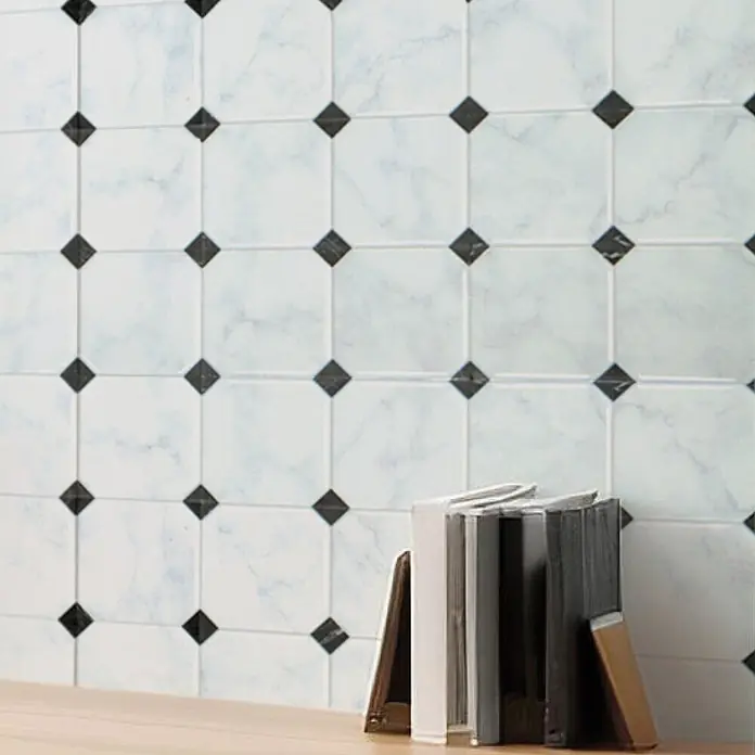 Smart Tiles Selbstklebemosaik Betera - 19,69 x 19,69 cm, Blanco, Glänzend - Weiße Wandfliesen in Marmoroptik mit schwarzen Rautenakzenten, an einer Wand hinter Büchern.