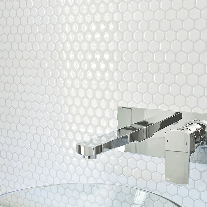 Smart Tiles Selbstklebemosaik Hexago - 24,46 x 28,6 cm, Weiss, Glänzend - Verchromte Wandarmatur mit Hebelgriff über einem Glaswaschbecken, vor weißen Sechseckfliesen.
