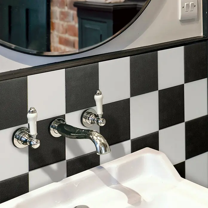 Smart Tiles Selbstklebemosaik Betera - 19,69 x 19,69 cm, Paris, Matt - Verchromte Wandarmatur mit weißen Keramikgriffen über einem weißen Keramikwaschbecken, Licht reflektierend.