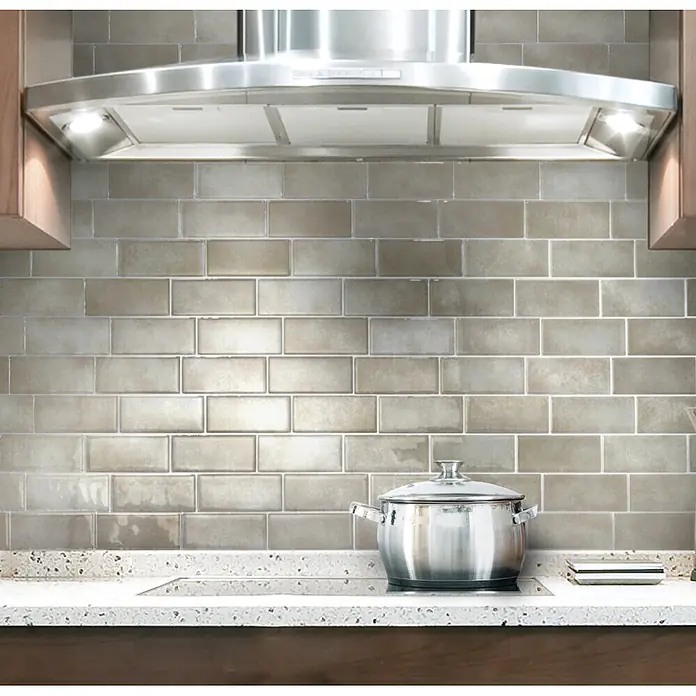 Smart Tiles Selbstklebemosaik Metro - 29,34 x 21,28 cm, Cologne, Glänzend - Hellgraue, glänzende Metrofliesen als Küchenrückwand unter einer Edelstahl-Dunstabzugshaube.