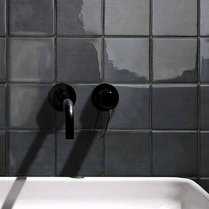 Smart Tiles Selbstklebemosaik Zellige - 22,86 x 22,86 cm, Taroudant, Glänzend - Schwarze wandmontierte Armatur und Griff auf dunkelgrauen Fliesen, über einem weißen Waschbecken.