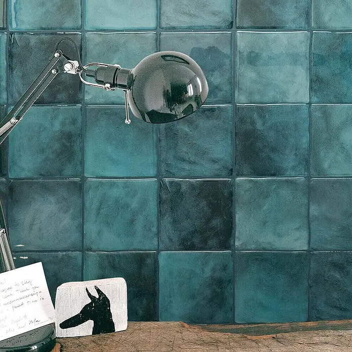 Smart Tiles Selbstklebemosaik Zellige - 22,86 x 22,86 cm, Costa, Glänzend - Türkisblaue quadratische Wandfliesen mit glänzender, handgefertigter Optik, die einen Bereich hinter einer Lampe verschönern.