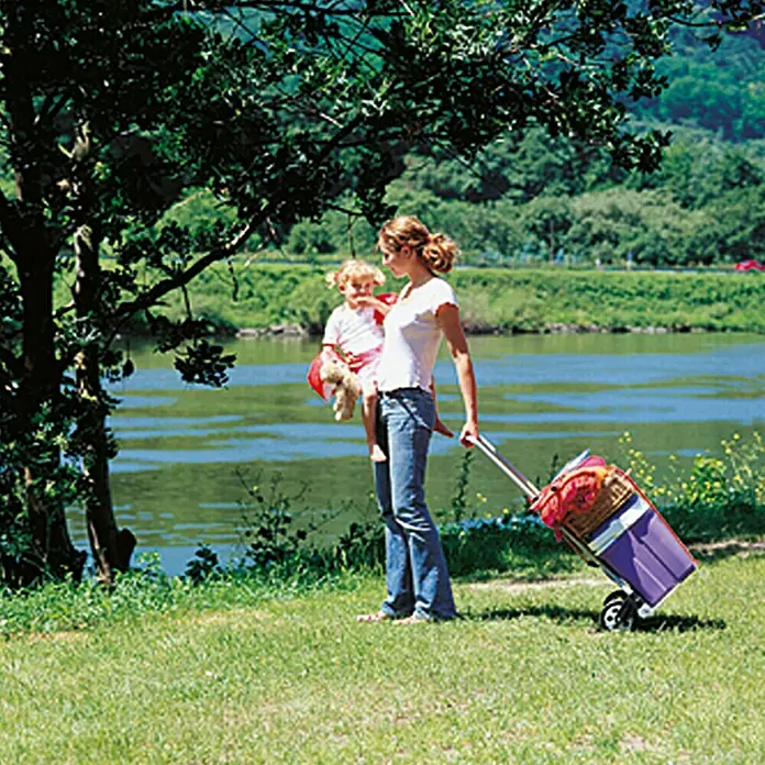 Wolfcraft Transportsystem TS 600 - 70 kg, Stufenlos höhenverstellbar - Frau mit Kind und lila Trolley am Seeufer. Der Trolley ist vollgepackt für einen Ausflug in die Natur.