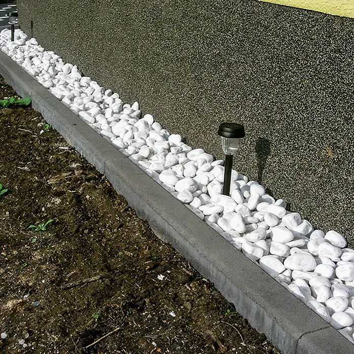 EHL Tiefbordstein - 100 x 25 x 8 cm, Grau, Beton - Nahaufnahme einer Bordsteinkante mit weißen Zierkieseln und kleinen Solarleuchten vor einer grauen Wand.