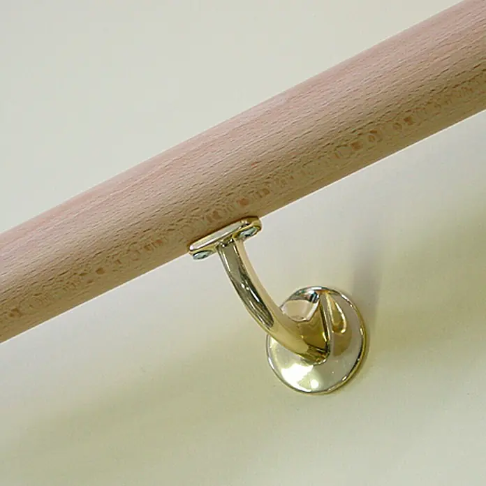 Treba Frewa Wandhalter B72 - Aluminium, Messing, 2 Stk. - Nahaufnahme einer hölzernen Treppengeländerstange, die mit einer eleganten goldenen Halterung an einer cremefarbenen Wand befestigt ist.