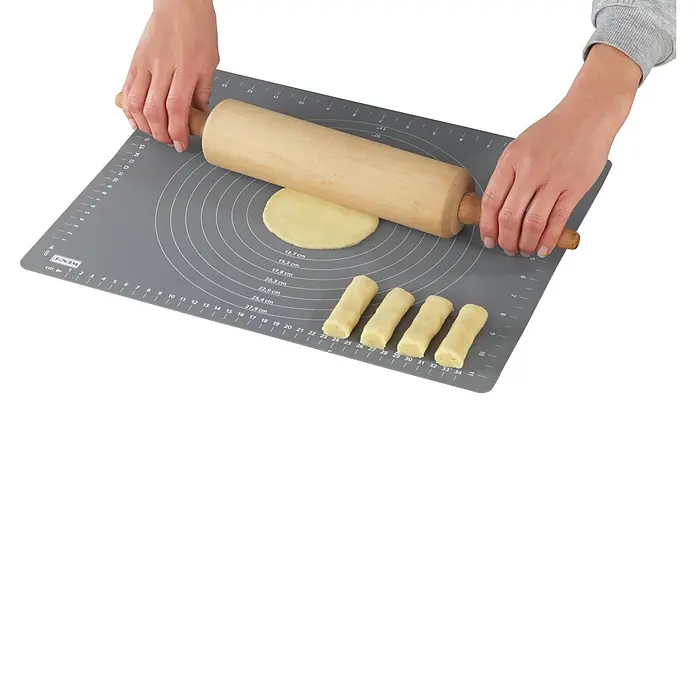 Wenko Silikonmatte - 340 x 30 mm - Hände rollen Teig mit einem Holz-Nudelholz auf einer grauen Silikon-Backmatte mit Maßen aus.
