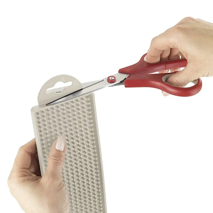 Wenko Abtropfmatte - 450 x 80 mm, Beige - Hände schneiden eine beige, strukturierte Matte mit roter Schere, zeigen flexibles Material und Verpackungslasche.