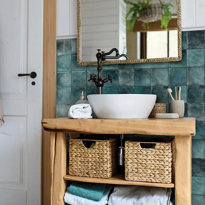 Smart Tiles Selbstklebemosaik Zellige - 22,86 x 22,86 cm, Costa, Glänzend - Holzbadezimmermöbel mit weißem Aufsatzwaschbecken, Bronzehahn und geflochtenen Körben.