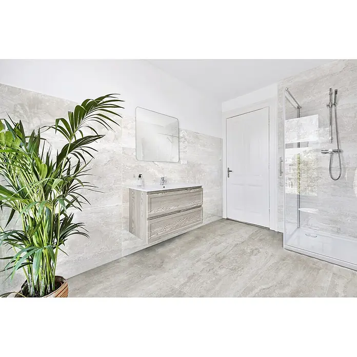 Feinsteinzeugfliese Trenova - 120 x 60 cm, Grigio, Glänzend - Modernes Badezimmer mit hellgrauen Marmor-Effekt-Fliesen an Wänden und Boden, dazu Waschtisch, Spiegel, Dusche und einer Pflanze.