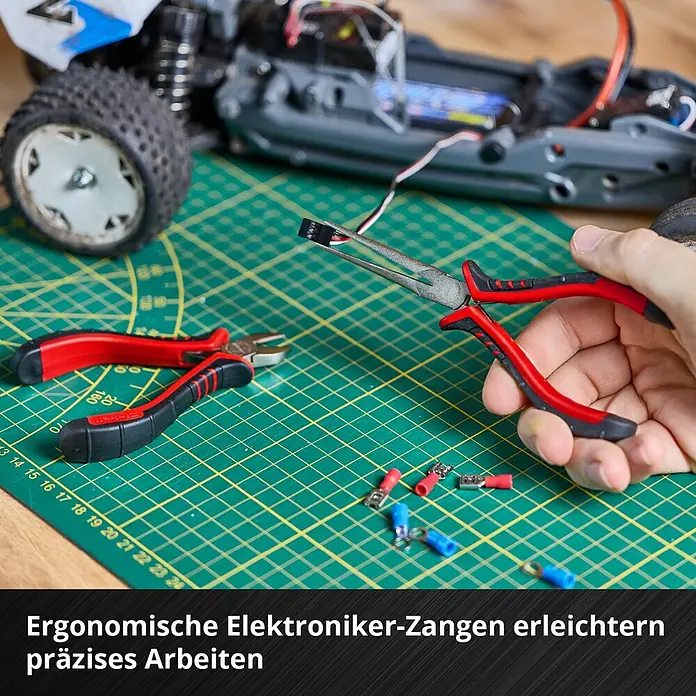 Einhell Werkzeugkoffer E-Case Hobby - 153 -tlg. - Ergonomische rot-schwarze Elektroniker-Zangen halten einen kleinen elektronischen Stecker während präziser Arbeiten an einem RC-Modell.