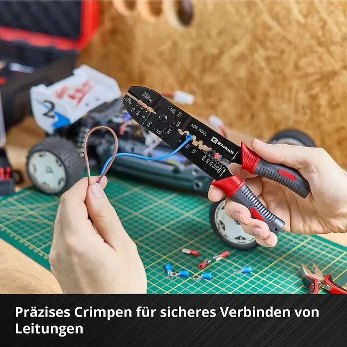 Einhell Werkzeugkoffer E-Case Hobby - 153 -tlg. - Hände verwenden eine schwarz-rote Crimpzange an einem blauen Draht, neben einem RC-Auto und Klemmen auf einer grünen Matte.