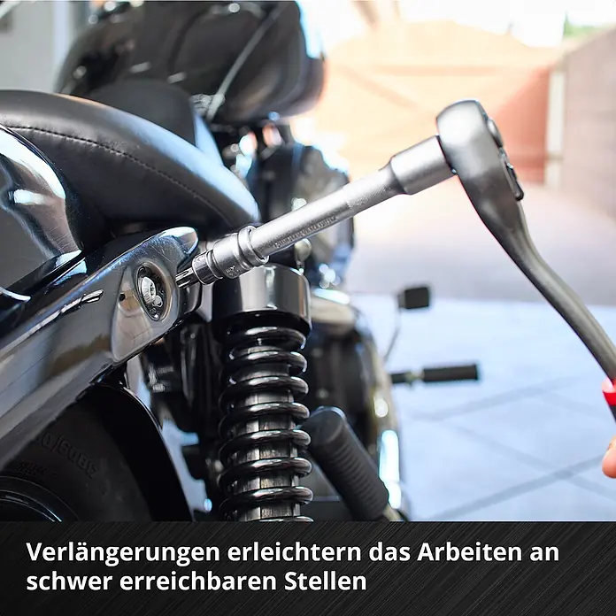 Einhell Werkzeugkoffer E-Case KFZ - 121 -tlg. - Metallische Ratsche mit Verlängerung und Torx-Bit, eingesetzt an einem Motorrad, um eine Schraube an schwer erreichbarer Stelle zu lösen.