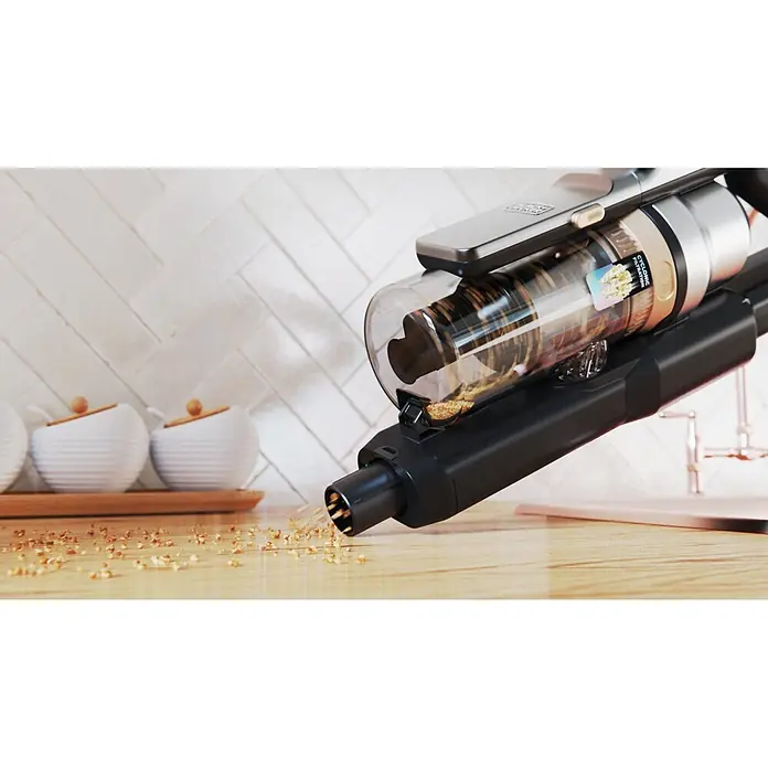 Black+Decker Aspirador de batería BSV525BLP-QW - 18 V, 1 batería, 2,5 Ah, Volumen de recipiente: 0,65 l - Una aspiradora de mano inalámbrica negra y plateada con un depósito transparente aspira pequeños residuos de una encimera de madera.