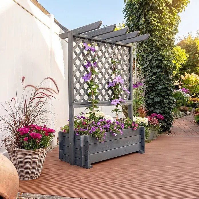 Promadino Pflanzkasten mit Pergola - Außenmaß (L x B x H): 140 x 64,5 x 102 cm, Holz, Grau - Grauer Holz-Pflanzkasten mit Spalier, gefüllt mit lila und weißen Blumen, auf einer Holzterrasse im Garten.