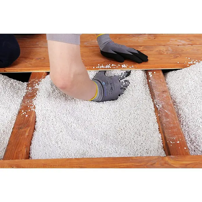 Knauf Isoself Hohlraumdämmung - 100 l - Ein Arbeiter füllt Perlit-Isolierung zwischen die Holzbalken eines Fußbodens, wobei er Handschuhe trägt, um die Hände zu schützen.