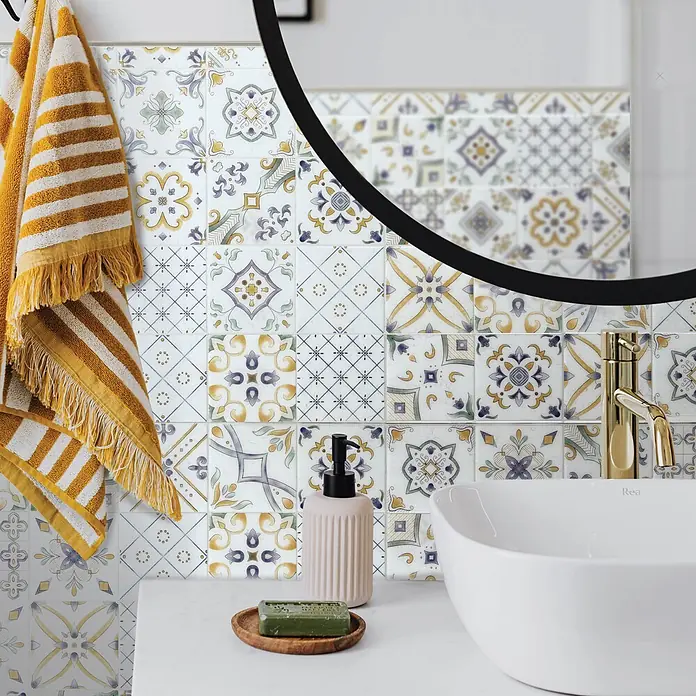Smart Tiles Selbstklebemosaik Vintage - 22,86 x 22,86 cm, Veletti, Glänzend - Bunt gemusterte Badezimmer-Wandfliesen im traditionellen Stil, hinter einem Waschbecken mit goldener Armatur und Spiegel.