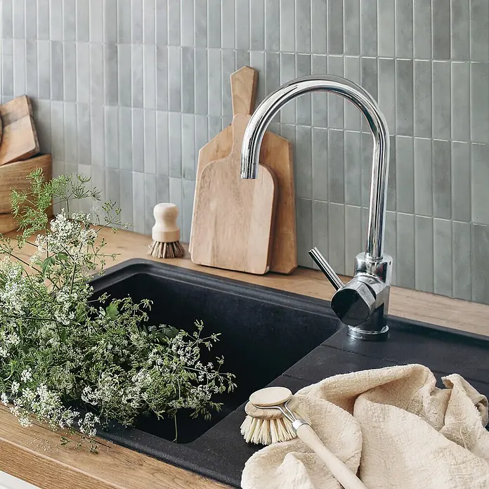 Smart Tiles Selbstklebemosaik Morocco - 29,02 x 22,86 cm, Casa, Glänzend - Stilvoller Küchenspülbereich mit schwarzem Becken, Chromarmatur, Holztheke, grüner Fliesenrückwand, frischen Kräutern und natürlicher Spülbürste.