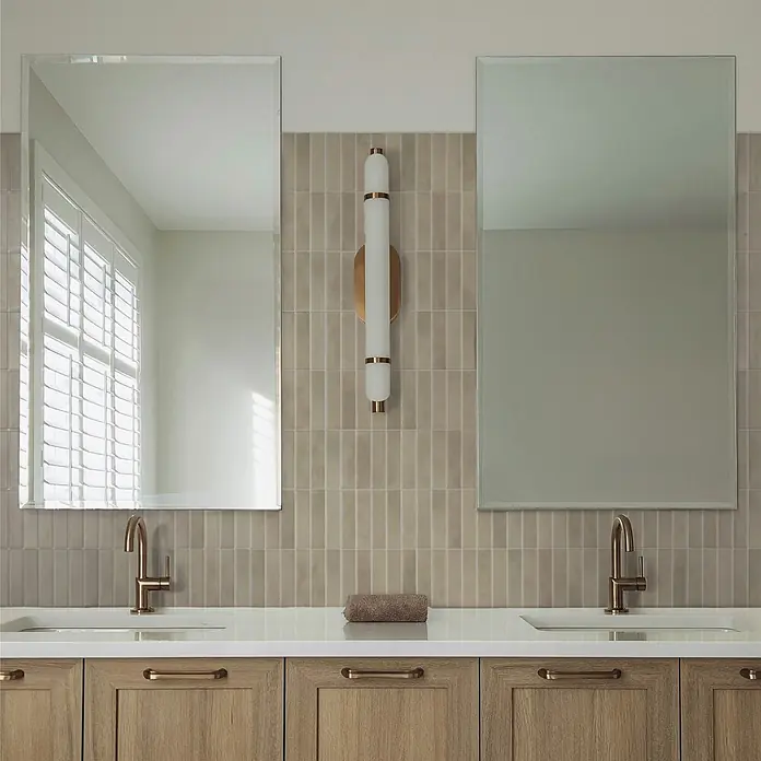 Smart Tiles Selbstklebemosaik Morocco - 29,02 x 22,86 cm, Tangier, Matt - Moderne Badezimmer-Doppelwaschtisch mit Holzschränken, weißer Arbeitsplatte, Bronze-Armaturen und rechteckigen Spiegeln über einer gefliesten Wand.