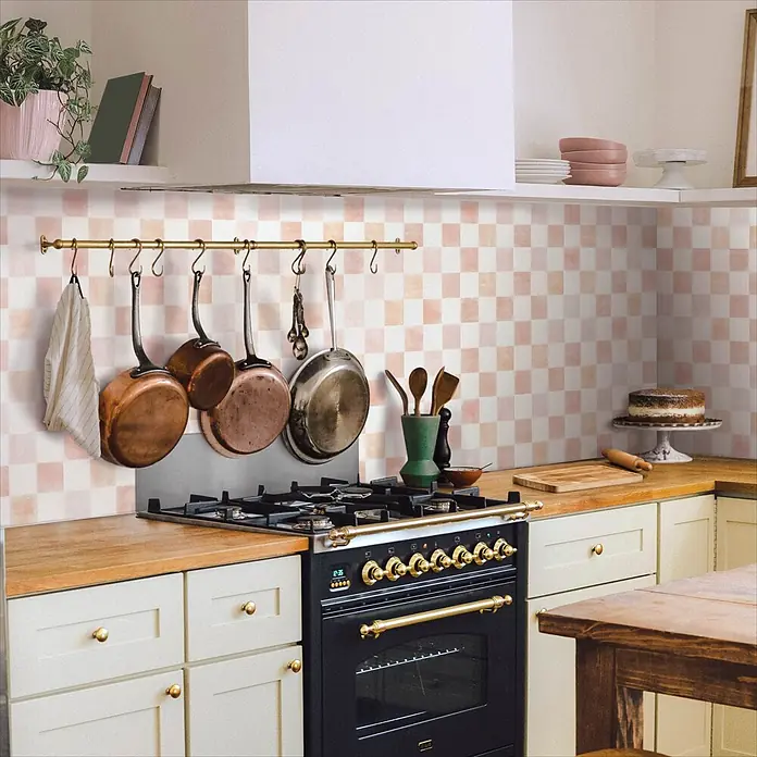 Smart Tiles Selbstklebemosaik Damier - 19,69 x 19,69 cm, Petra, Matt - Hellrosa und weiß karierte Küchenrückwandfliesen mit hängenden Töpfen über einem Herd.