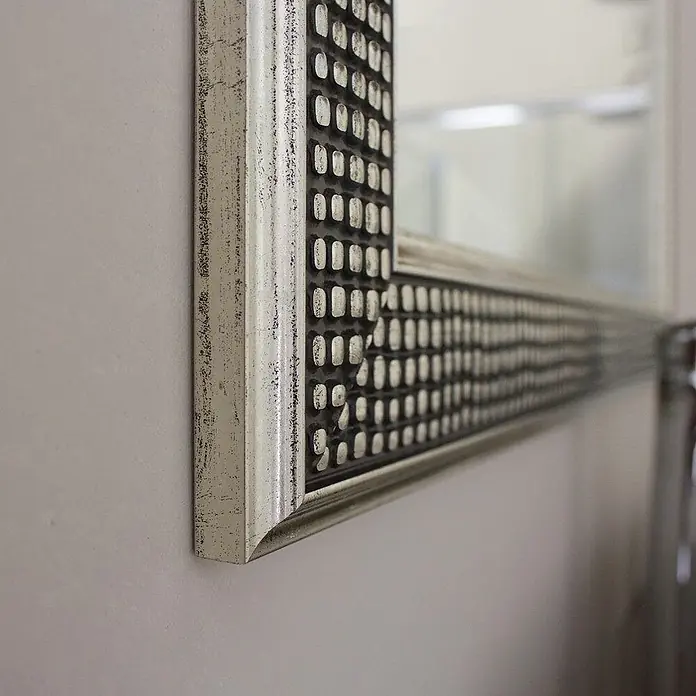 Kiamami Valentina Lichtspiegel - 22 x 645 cm, Farblos - Antik silberner Spiegelrahmen mit strukturierter Oberfläche aus erhabenen hellen Rechtecken und dunklen Vertiefungen an einer Wand.