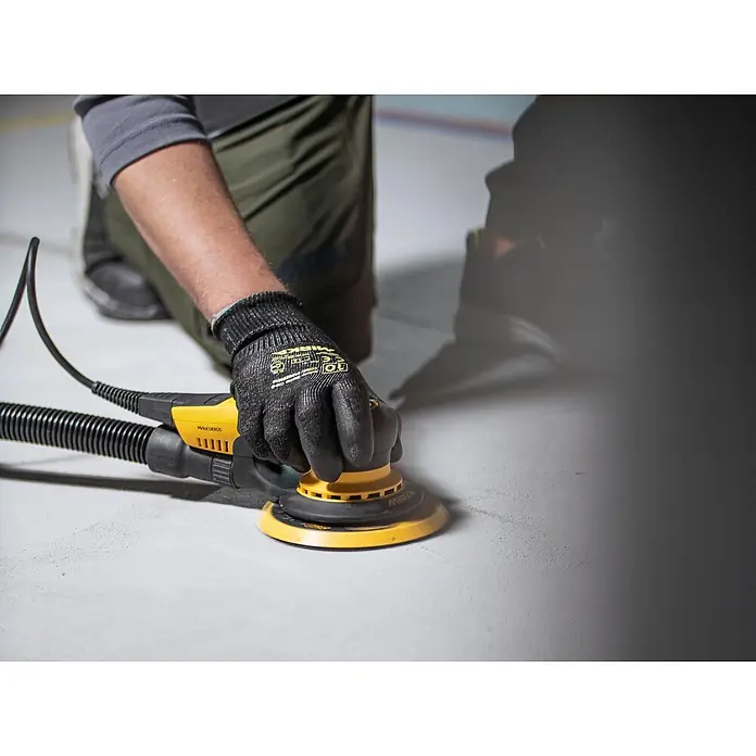 Mirka Elektro-Exzenterschleifer Mirka® DEROS II 650 150mm Hub 5,0 - 400 W, 4.000 U/min - 10.000 U/min, Durchmesser Schleifteller: 15 cm - Person nutzt einen gelb-schwarzen Exzenterschleifer mit Absaugschlauch zum Schleifen einer hellen Oberfläche.