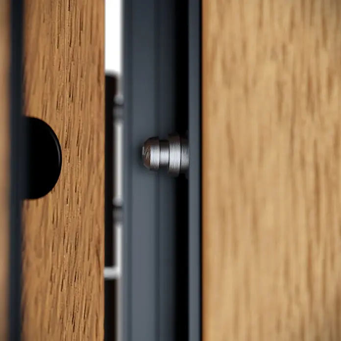 FM Türen Haustür - 110 x 210 cm, DIN Anschlag: Links, Winchester, Mit vertikaler Verglasung + Zierapplikationen - Nahaufnahme eines silbernen Sicherungsstifts am Türband einer Holztür, teilweise geöffnet.