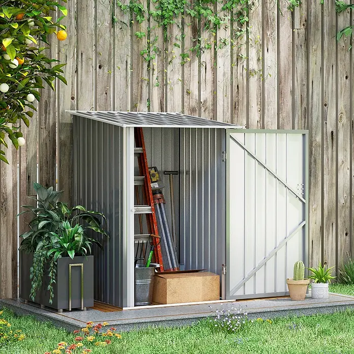 SONNENH Gerätehaus - Außenbreite inkl. Dachüberstand: 100 cm, Außentiefe inkl. Dachüberstand: 103 cm, Stahl, Grau - Grauer Metall-Gartenschuppen mit Werkzeugen, offener Tür, im Garten neben einem Holzzaun und Pflanzen.