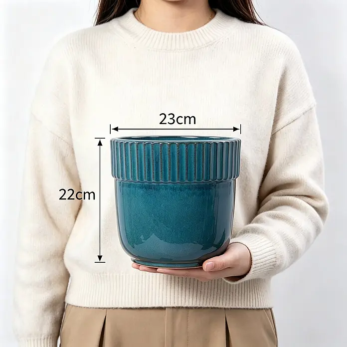 SONNENH Pflanztopf - 1 Stk., Keramik, Blau - Glänzender blauer Keramik-Pflanztopf, 23 cm breit und 22 cm hoch, mit geripptem Detail, von einer Person gehalten.