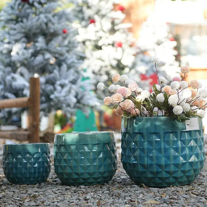 SONNENH Pflanztopf - 3 Stk., Keramik, Blau - Drei teal-farbene Keramik-Pflanzgefäße mit geometrischem Muster; das größte mit hellrosa und weißen Blumen, im Freien auf Kies.
