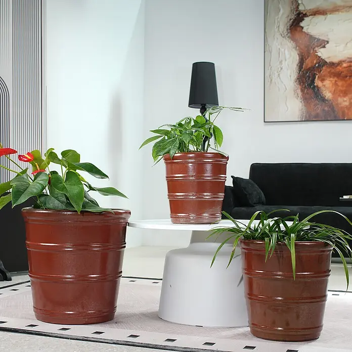 SONNENH Pflanztopf - 3 Stk., Keramik, Braun - Drei glänzende, braune, fassförmige Pflanzgefäße mit verschiedenen Grünpflanzen und roten Blumen in einem modernen Wohnzimmer.