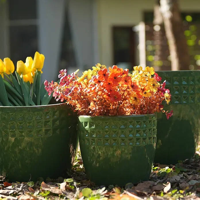 SONNENH Pflanztopf - Keramik, Grün - Drei glänzend grüne Pflanzgefäße mit geometrischer Textur, gefüllt mit gelben Tulpen und warmfarbigen Blumen, draußen.