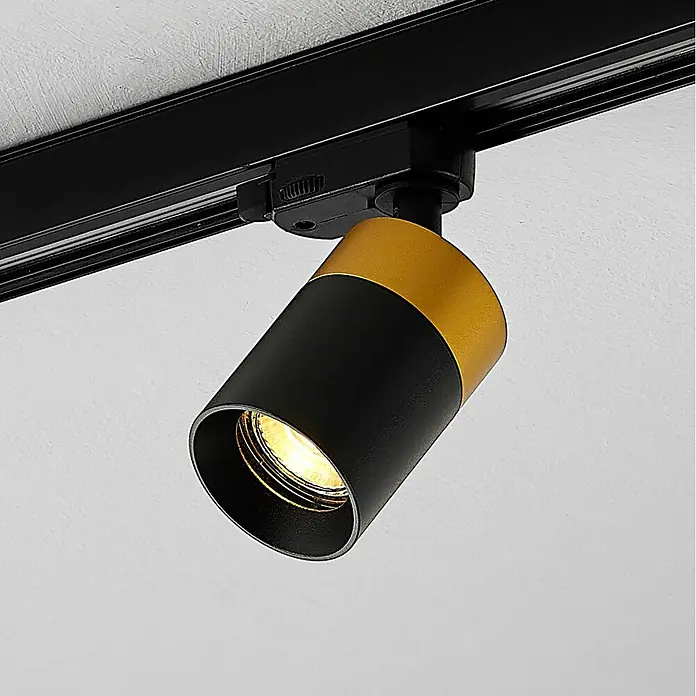 Arcchio LED-Spannseilsystem Nikora - schwarz, schwarz - Schwarz-goldene Stromschienenleuchte, an einer Schiene montiert, die warmes Licht abstrahlt.
