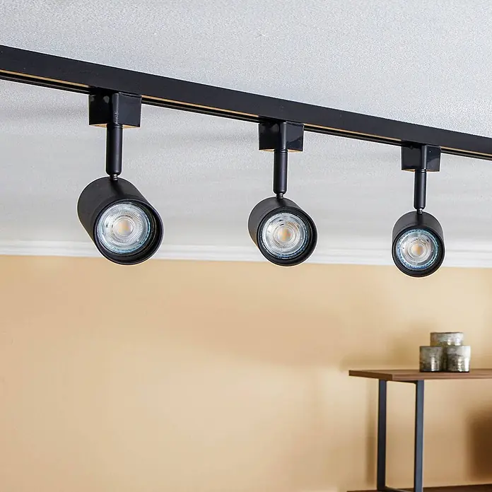 Prios LED-Spannseilsystem Jorell - schwarz, schwarz - Schwarze Stromschiene mit drei Strahlern an der Decke, beleuchtet einen Raum in warmen Tönen.